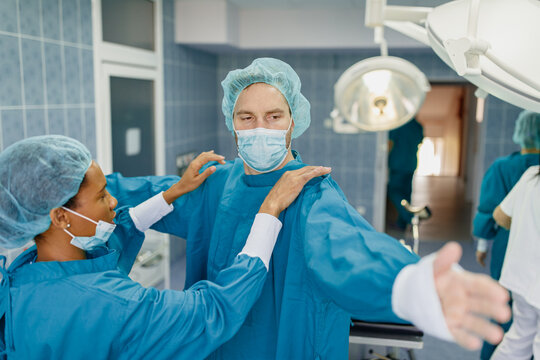 Healthcare Professional Team Assisting Surgeon With Sterile Protective Gear In Bright Operating Room Environment - Powered by Adobe