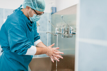Caucasian Male Doctor Washing Hands in Blue Surgical Scrubs Under Bright Lighting