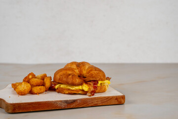 Bacon, egg and cheese croissant with hash brown rounds on wood cutting board 