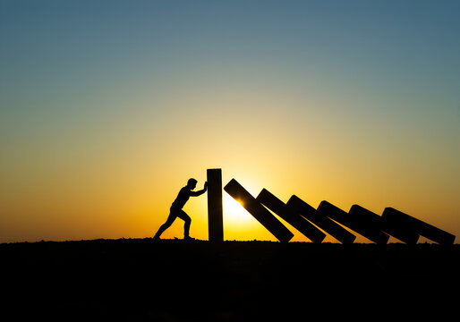 Silhouette of man pushing falling dominoes at sunset