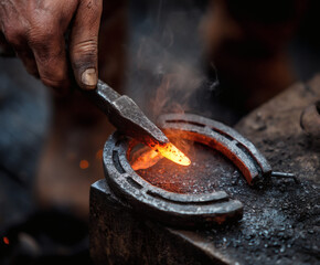 A blacksmith meticulously shapes a red-hot horseshoe with precision and skill in his workshop.