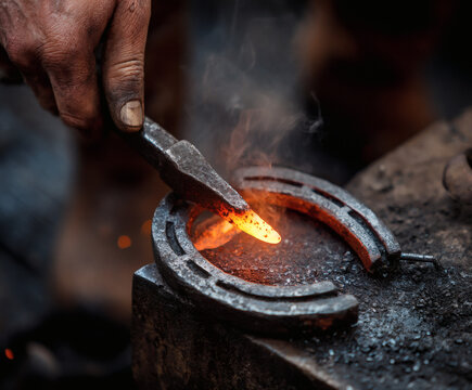 A blacksmith meticulously shapes a red-hot horseshoe with precision and skill in his workshop.