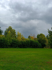 Obraz premium Dramatic cloudy sky over a harvested field and green meadow in the countryside, capturing the contrast between summer crops and approaching autumn weather.