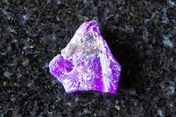 sample of rough sugilite mineral on black granite