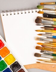 Top View of Watercolor Brushes, Paints, and Sketchbook on Clean White Background