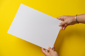 Hands Holding Blank White Sheet on Yellow Background