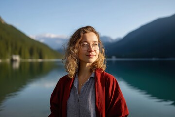 Fototapeta premium Young caucasian female posing by scenic mountain lake in red jacket