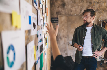 Focused male entrepreneur listening to UX strategy pitch, analyzing complex data wall with user...