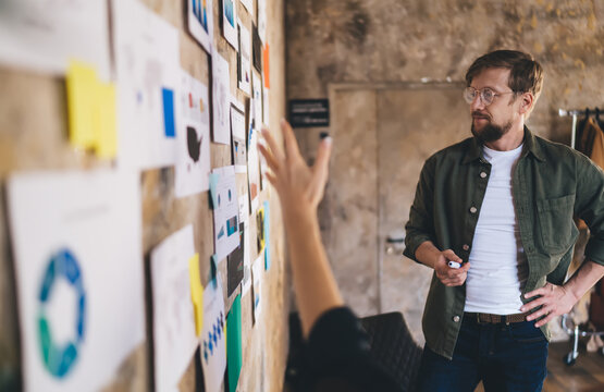 Focused male entrepreneur listening to UX strategy pitch, analyzing complex data wall with user insights and tech diagrams during planning sprint in modern workspace.