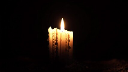 A candle with melted wax dripping down the sides and a bright flame in a dark background view - Powered by Adobe