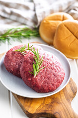 Raw burger beef patties on plate on white table.