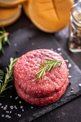 Raw burger beef patties on cutting board on black table.