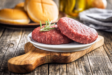 Raw burger beef patties on plate on wooden table.