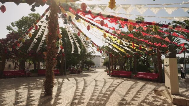 Colorful festival streamers casting shadows in a sunlit town square, Algarve, Portugal