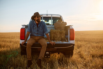 Happy farmer relaxing in back of his truck in field. © Drazen