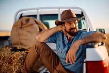 Naklejka premium Pensive man relaxing in back of his truck on farm field.