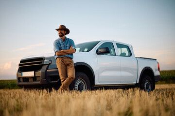 Happy farmer with arms crossed leaning on pick-up truck in field. © Drazen