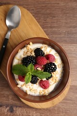 Tasty yogurt with granola and berries in bowl on wooden table, top view