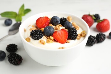 Tasty yogurt with granola and berries in bowl on white table, closeup