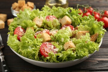 Tasty salad with croutons, tomatoes, cheese and chicken on black wooden table, closeup