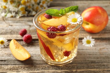 Iced tea. Refreshing drink with peach, raspberries and chamomiles on wooden table, closeup