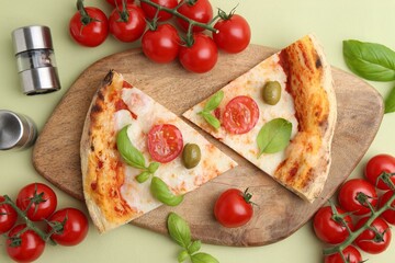 Pieces of delicious pizza, tomatoes and basil on light green background, flat lay
