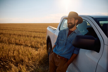 Happy farm worker leaning on his truck while spending day in field. © Drazen