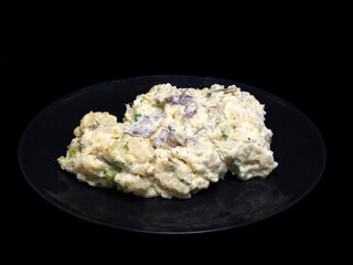 Potato salad on a black plate against a black background