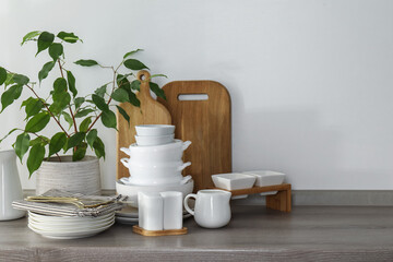 Different clean white dishware, wooden cutting boards, cutlery and houseplant on counter in kitchen