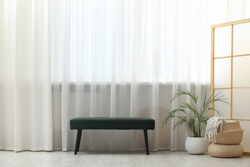 Stylish furniture and houseplant near window with curtains in living room. Interior design