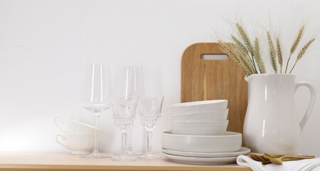 Fototapeta premium Different clean white dishware, cutlery, cutting board, glasses and spikes on wooden table indoors