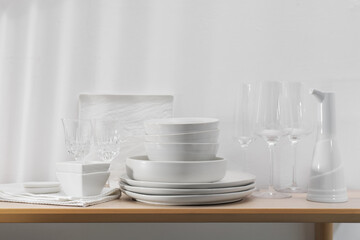 Different clean white dishware and glasses on wooden table indoors