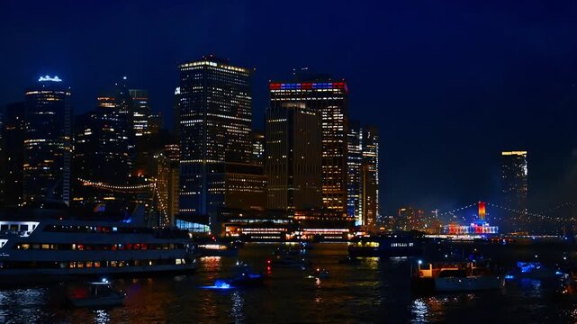 Gorgeous night skyline of New York, USA. View from the riverscape where multiple boats gathered. Fireworks flashes at backdrop.