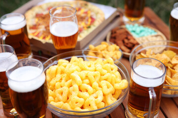 Glasses of beer and different snacks on wooden table outdoors, closeup