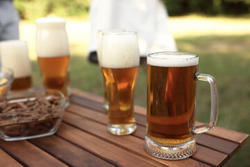 Glasses of beer and snacks on wooden table outdoors, closeup