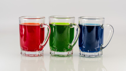 Three Glass Mugs Filled with Red, Green, and Blue Colorful Beverages on White Background
