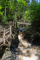 Rushing water at Bushkill Falls after significant spring rainfall with wooden boardwalk alongside.
