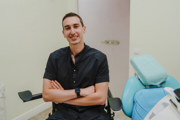 A young smiling dentist at his workplace. Specialist in oral cavity treatment. A doctor in a black uniform. A doctor with a watch on his right hand. Interior of a dental office.