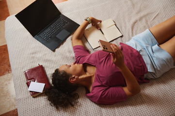 Woman Relaxing on Bed While Using Smartphone and Notebook for Work