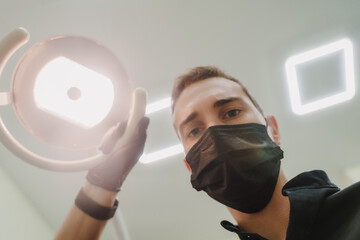 The dentist looks at the camera and shines a lamp.