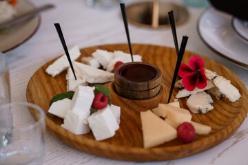 Gourmet Cheese Board with Central Dip, Raspberries, and Flowers on Wooden Surface, Brightly Lit Table Setting.
