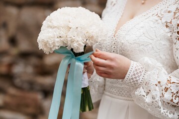 Bride Holding Cream White Carnation Bouquet with Blue Ribbon, Wedding Lace Dress, Romantic Stone Wall Backdrop