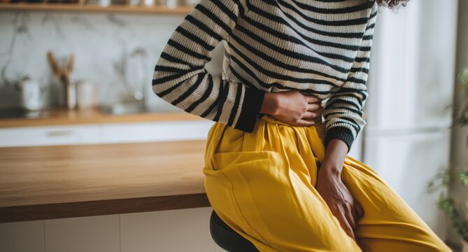 A close-up shot of an African American woman sitting on the edge of her kitchen barstool holding onto one side of her stomach in pain Generative AI