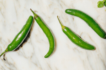 four green serrano chili peppers on white marble