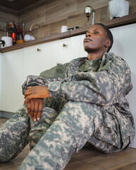 Fototapeta premium Depressed african american soldier sitting on kitchen floor