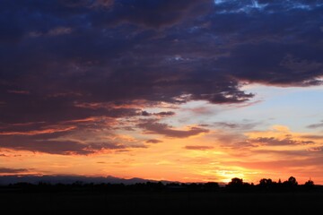 Obraz premium Vivid sunset spectacle painting the sky with orange, purple, and gold hues over the silhouetted horizon, perfect for backgrounds.