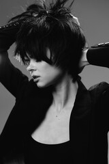 Naklejka premium Black and white portrait of a young woman with short hair posing with raised arms in stylish dark clothing
