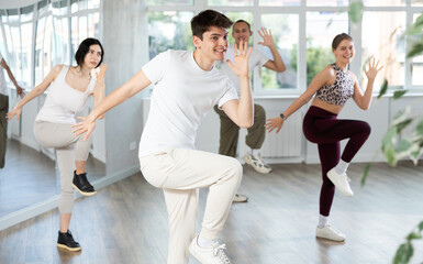 Happy young man in sportswear with group practising charleston dancing in modern dance hall
