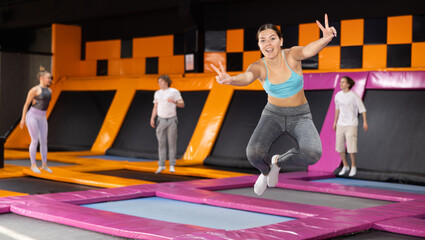 Obraz premium Dynamic young woman wearing sport clothes high jumping in trampoline arena
