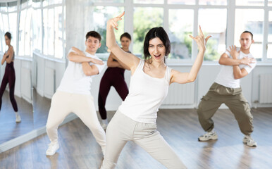 Fototapeta premium Positive enthusiastic young dark-haired woman learning modern street dancing during group class in choreographic studio..